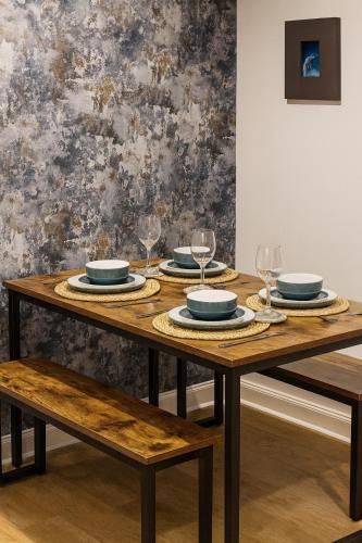 a wooden table with plates and wine glasses on it at Erskine Apartment-Small and Cosy 1 Bedroom Apartment in Angus