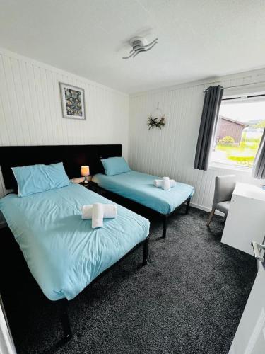 a bedroom with two beds with blue sheets and a window at Tigh Na Mara in Dunoon