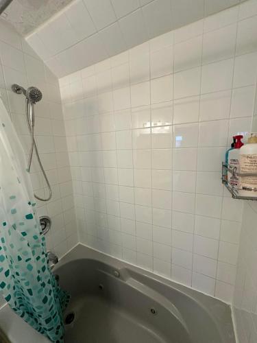 a bathroom with a tub and a white tiled wall at Goldwin's Place in Toronto