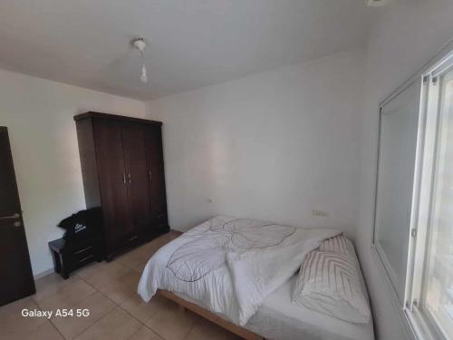 a white bedroom with a bed and a wooden cabinet at יחידת נוף לגלבוע in Bet Sheʼan