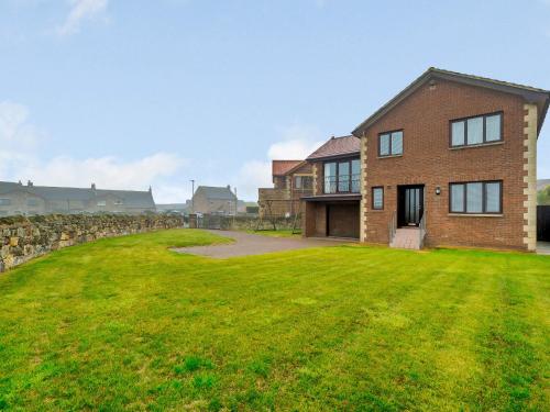 a brick house with a large lawn in front of it at Seaglass House in Beadnell