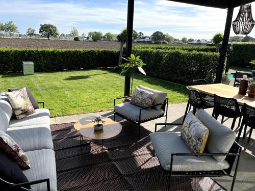 a patio with couches and a table and a table and grass at Pool, Spa pool, Private, Modern, Clive! in Clive