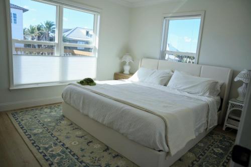 a bedroom with a large white bed with two windows at Sea'scape - Heated Pool, Beach Gear, Pet Friendly, Beach Views in Pensacola Beach