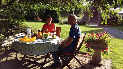 Un hombre y una mujer sentados en una mesa en Chambres d'hôtes La Pinderie, en Val Couesnon