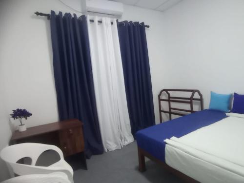 1 dormitorio con cortinas azules, 1 cama y 1 silla en Casa Tranquila, en Talalla South
