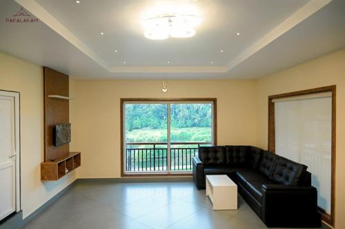 a living room with a black couch and a large window at Pakalakam Resorts in Cheruppulasseri