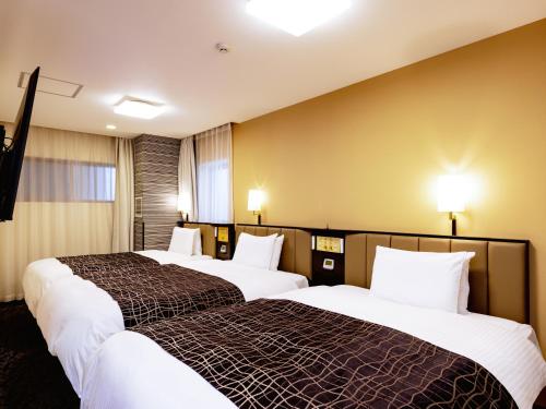 two beds in a hotel room with a cross on the wall at APA Hotel Saga Ekimae Chuo in Saga