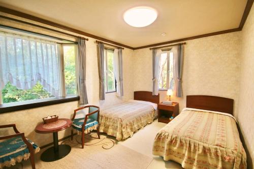 a bedroom with two beds and a table and a chair at 風薫る宿 伊豆星の舞 in Ito