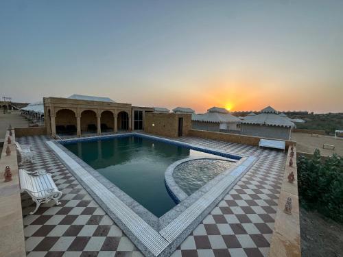 a pool on a resort with a sunset in the background at The Mayara Fort Jaisalmer Camps in Jaisalmer