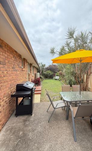 a patio with a table and an umbrella and a grill at Forster Holiday Home Cozy, Central & Near Beach in Forster