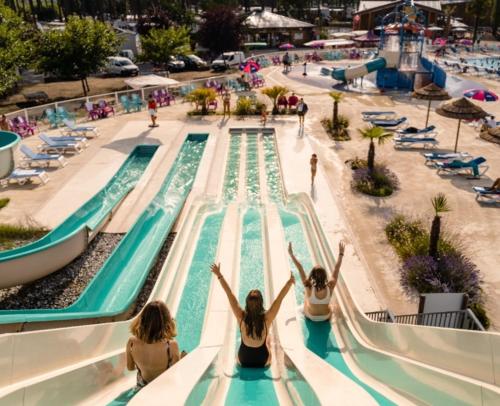 three women sitting on a water slide at a swimming pool at Mobil-home neuf sous les pins, à proximité des infrastructures in Saint-Julien-en-Born