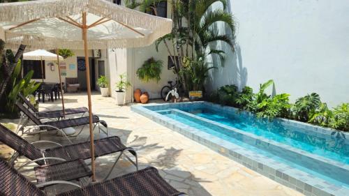 a pool with chairs and an umbrella next to a building at Graciosa Suites in Praia do Frances