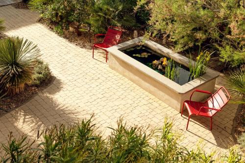 two red chairs and a pond in a garden at Hotel de La Plage in Contis-les-Bains