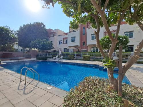 a swimming pool with a tree in front of a building at Peaceful and Spacious 2 BDR in the Heart of Al Ghadeer Community in Ghantoot