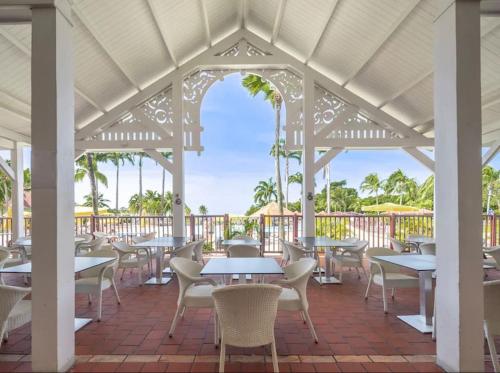 um pátio com mesas, cadeiras e palmeiras em Suite Paradis Village Vacances Vue mer & piscine em Sainte-Luce