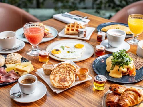 a wooden table topped with plates of breakfast food at Le Louise Hotel Brussels - MGallery Collection in Brussels