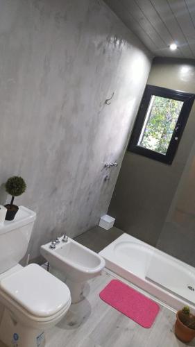 a bathroom with a toilet and a tub and a window at Vida en el bosque in Necochea