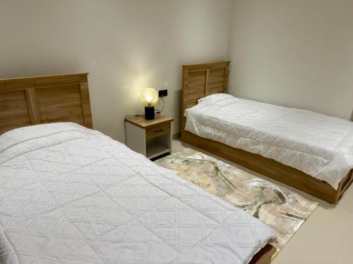two beds in a bedroom with a lamp on a table at Al Furat Apartment in Seeb