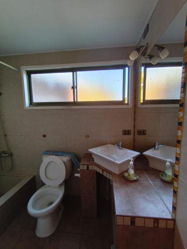a bathroom with two sinks and a toilet and two windows at Cabaña en cahuil pichulemu in Cáhuil