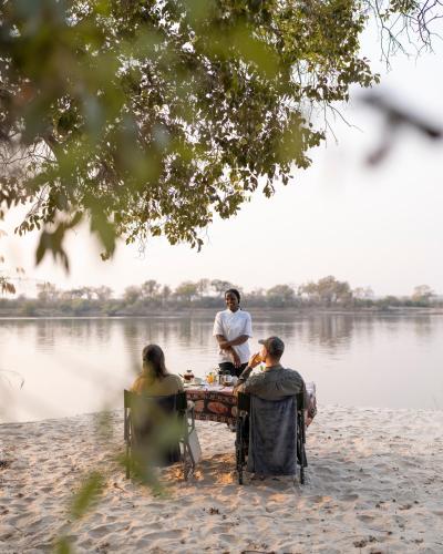 a group of people sitting around a table by the water at Zambezi Dusk River Facing-all inclusive-Luxury Accommodation in Livingstone