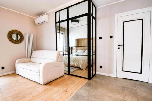 a living room with a white chair and a bedroom at Marina Ostróda III - widok na jezioro, podziemny garaż, winda, klimatyzacja, wanna i prysznic, 2 łazienki, lux in Ostróda