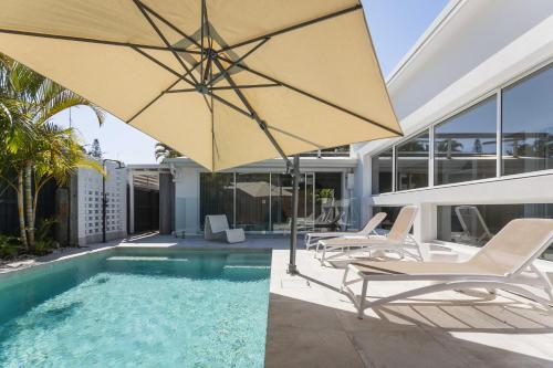 サンライズ・ビーチにあるA beautiful Noosa Gem in Sunrise Beachの家の隣に椅子とパラソル付きのプールがあります。