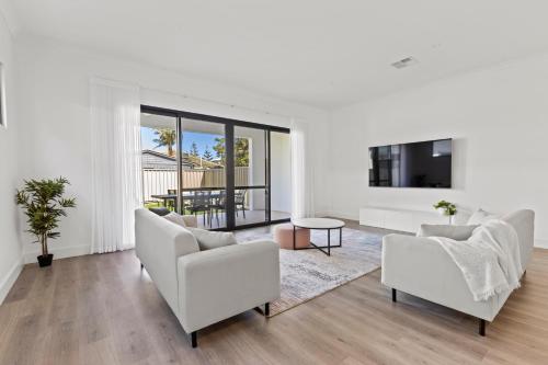 a living room with white furniture and a flat screen tv at Swainson on 3 Lexington - 200m to Beach! in Henley Beach