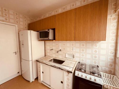 a kitchen with a white refrigerator and a stove top oven at AP localização é tudo Pitangueiras in Guarujá