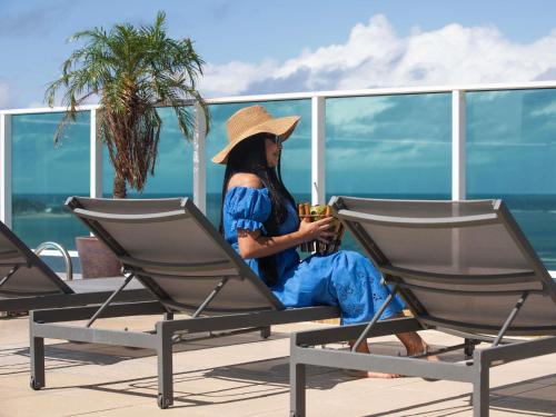 a woman sitting on a deck with a drink at Mercure Maceio Pajuçara in Maceió