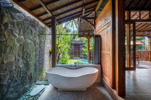 a bath tub in a room with a stone wall at Anggi Villas Ubud in Tegalalang