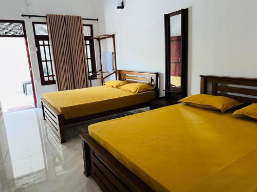 two beds in a room with yellow sheets at Nishadi Holiday Inn Kataragama in Kataragama