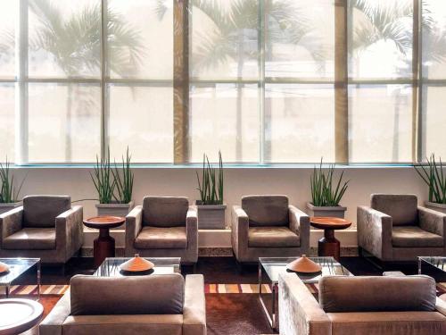 a waiting room with couches and chairs and palm trees at Mercure Salvador Pituba in Salvador