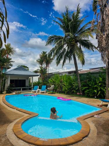 a woman swimming in a pool with palm trees at Sansuko Ville Panwa in Ban Bo Rae