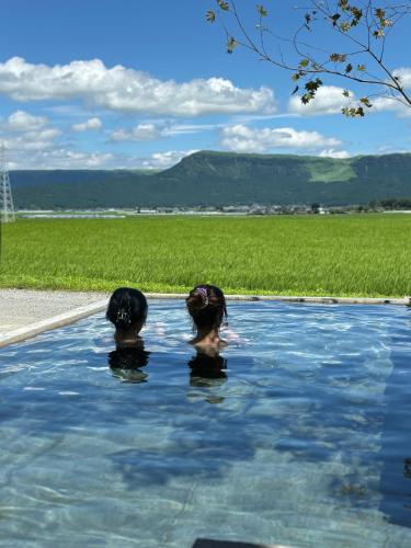 dwie osoby w basenie z polem w tle w obiekcie 大観峰と阿蘇山を望む!!二棟のプレミアム古民家宿 w mieście Aso