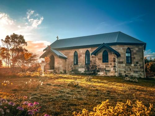an old church on a field with flowers at St Martins of Tasmania - converted heritage listed church in Dunalley