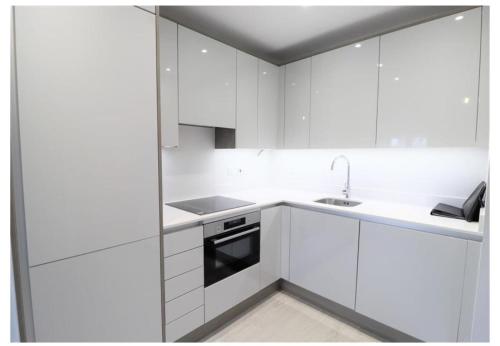 a white kitchen with white cabinets and a sink at Charming 1 Bedroom Flat in the Heart of Uxbridge in Uxbridge