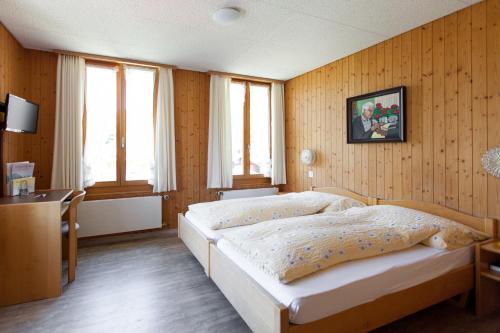 a bedroom with a bed and a desk and windows at Hotel Edelweiss in Wengen