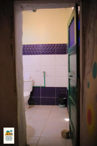 a bathroom with a toilet and purple and white tiles at Heissa Nubian Hostel in Aswân Reservoir Colony