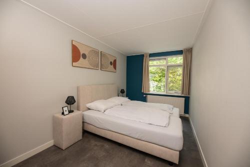 a bedroom with a white bed and a window at Luxe 12-persoons Groepsvilla – Gelijkvloers met Tuin & Loungeset in Apeldoorn