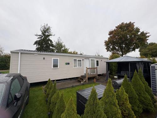 a small white caravan with a deck and a house at Chalet Meerwijck mit Terrasse am Wasser und Meer mit Schwimmbad in Kropswolde
