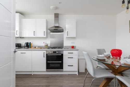 a kitchen with white cabinets and a table with chairs at Spacious Milton Keynes Townhouse 2 Designated Parking Spaces Near Centre MK, MK Bowl, Universal Studios & Transport Links Ideal for Families & Contractors in Milton Keynes