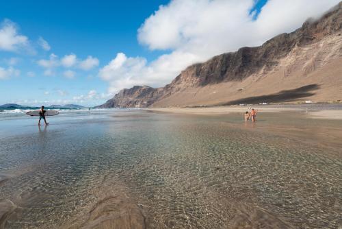 a man walking on the beach with a surfboard at Lanzarote Famara Beach Bungalow in Famara