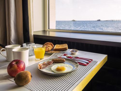 Una mesa de desayuno con huevos y pan y vista al océano. en Hotel Mercure Roscoff Bord De Mer, en Roscoff