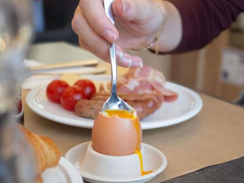 a person is eating an egg with a fork at Novotel Narbonne Sud A9/A61 in Narbonne
