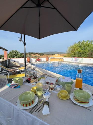 een tafel met eten en drinken en een parasol naast een zwembad bij Monte da Freira in Bencatel