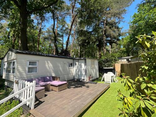 a tiny caravan with a deck in a yard at Tante Truus - Gezellig huisje op kindvriendelijk vakantiepark met zwembad in Hoenderloo