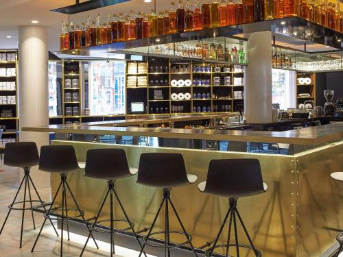 a bar with black stools in front of a counter at INK Hotel Amsterdam - MGallery Collection in Amsterdam