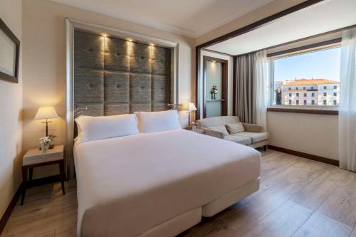 une chambre avec un grand lit blanc et une fenêtre dans l'établissement NH Collection A Coruña Finisterre, à La Corogne