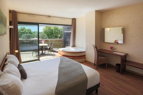 a hotel room with a bed and a desk and a balcony at Ile du Gua Suites in Narbonne