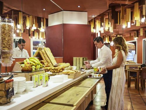 Un hombre y una mujer de pie en una cocina preparando comida. en ibis Thalassa Hyeres Plage, en Hyères